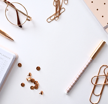 desk with glasses, pen, paperclips, note pad, and pins